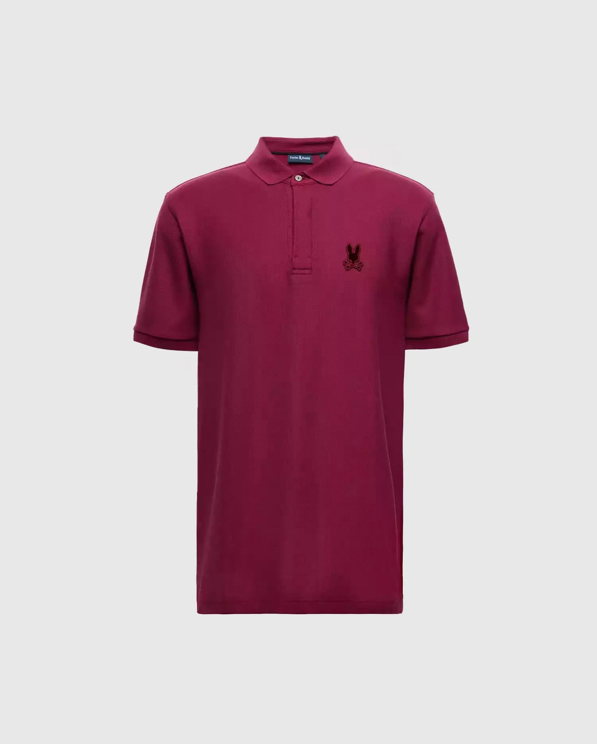 Introducing the Psycho Bunny Men's Branson Pique Polo - B6K108E200: a luxurious maroon polo shirt crafted from Pima cotton, complete with short sleeves and a collar. It features a small embroidered logo on the left chest, providing an elegant contrast against the plain light gray backdrop.