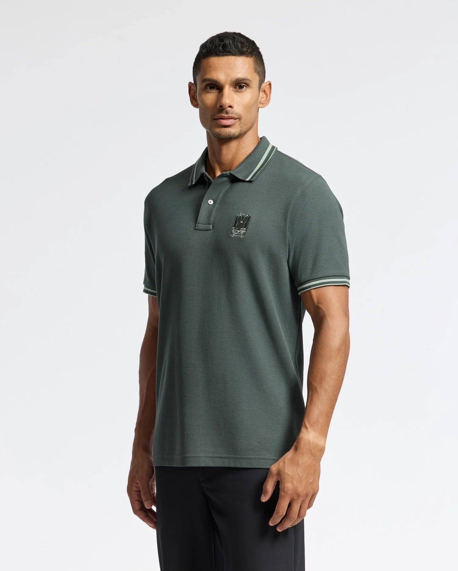 A man wearing a Psycho Bunny MENS PIERCE PIQUE POLO - B6K201E200 poses against a plain white background.