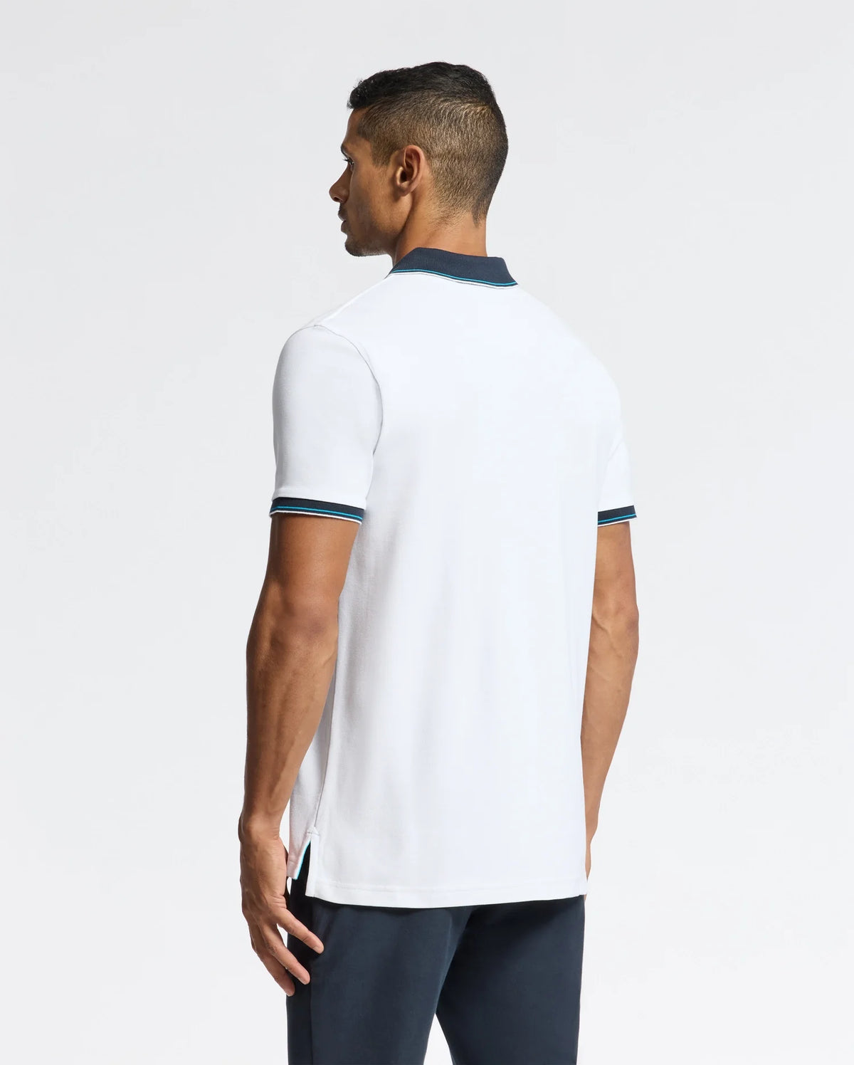 A person stands facing away, wearing a Psycho Bunny MENS BRANDON PIQUE POLO - B6K280E200 featuring premium quality and dark trim on the collar and sleeves, paired with dark pants. The luxurious polo is showcased against a plain white background, highlighting the outfit.