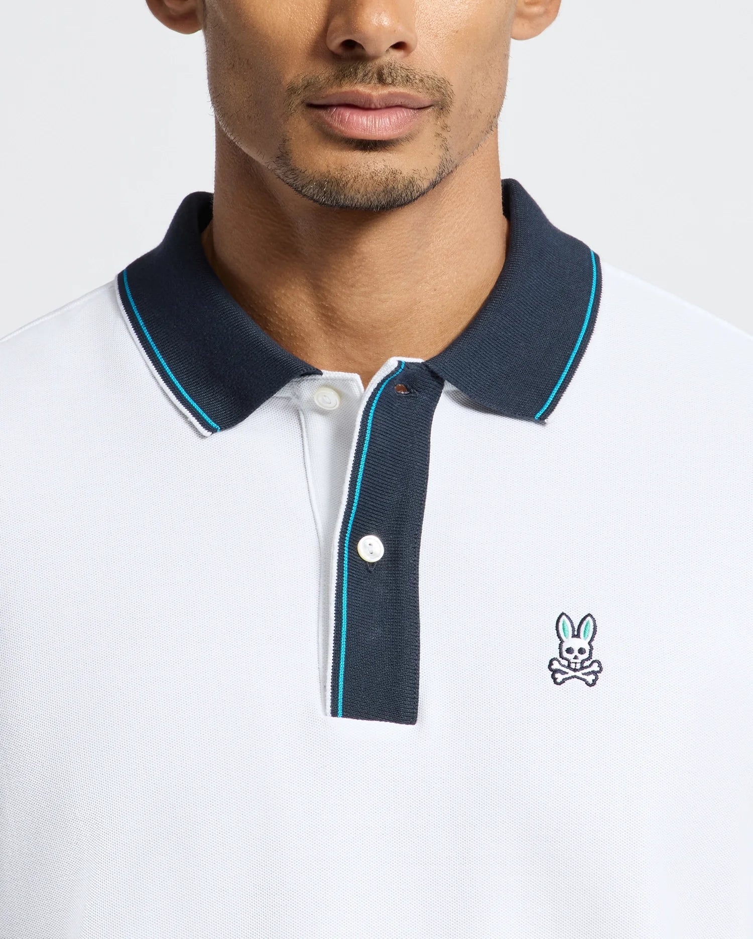 A man wears the exclusive Psycho Bunny MENS BRANDON PIQUE POLO - B6K280E200, distinguished by its black collar and a subtle embroidered rabbit logo on the chest. This luxurious pique polo delivers a modern, casual style ideal for any occasion.