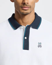 A man wears the exclusive Psycho Bunny MENS BRANDON PIQUE POLO - B6K280E200, distinguished by its black collar and a subtle embroidered rabbit logo on the chest. This luxurious pique polo delivers a modern, casual style ideal for any occasion.