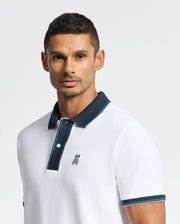 A man is dressed in the stylish MENS BRANDON PIQUE POLO by Psycho Bunny, featuring a dark collar and a discreet embroidered logo on the chest. He has short dark hair and a well-maintained beard, posing against a simple light background.