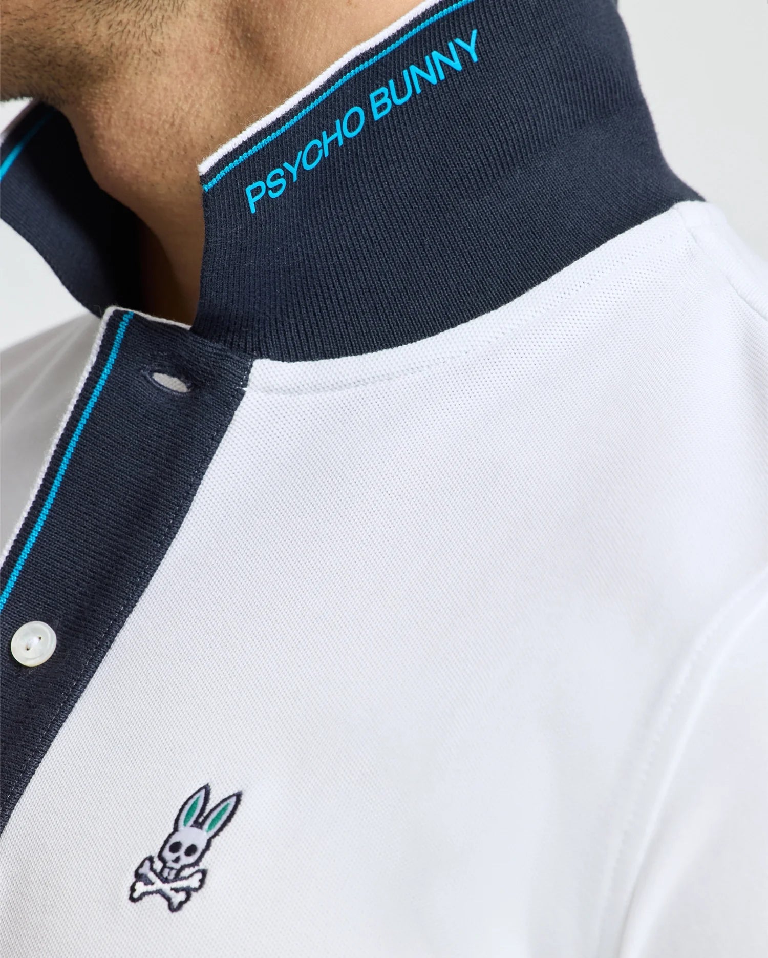 Indulge in the luxurious feel of the Psycho Bunny Men's Brandon Pique Polo - B6K280E200. This premium white Pima cotton polo stands out with its striking black collar adorned with blue "PSYCHO BUNNY" text, highlighted by blue and white trim on the button placket. The signature bunny with crossbones logo graces the chest, adding a distinctive touch.