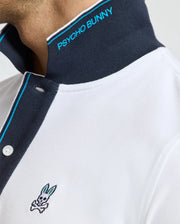 Indulge in the luxurious feel of the Psycho Bunny Men's Brandon Pique Polo - B6K280E200. This premium white Pima cotton polo stands out with its striking black collar adorned with blue "PSYCHO BUNNY" text, highlighted by blue and white trim on the button placket. The signature bunny with crossbones logo graces the chest, adding a distinctive touch.