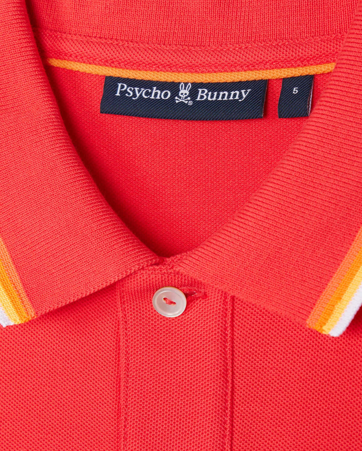 Close-up of the collar of the red Psycho Bunny MENS GRANBURY PIQUE POLO - B6K400C200, featuring a button at the top. The rib knit collar showcases orange, white, and yellow stripes along the edge. Inside the collar, a black label displaying the brand name and logo is visible.