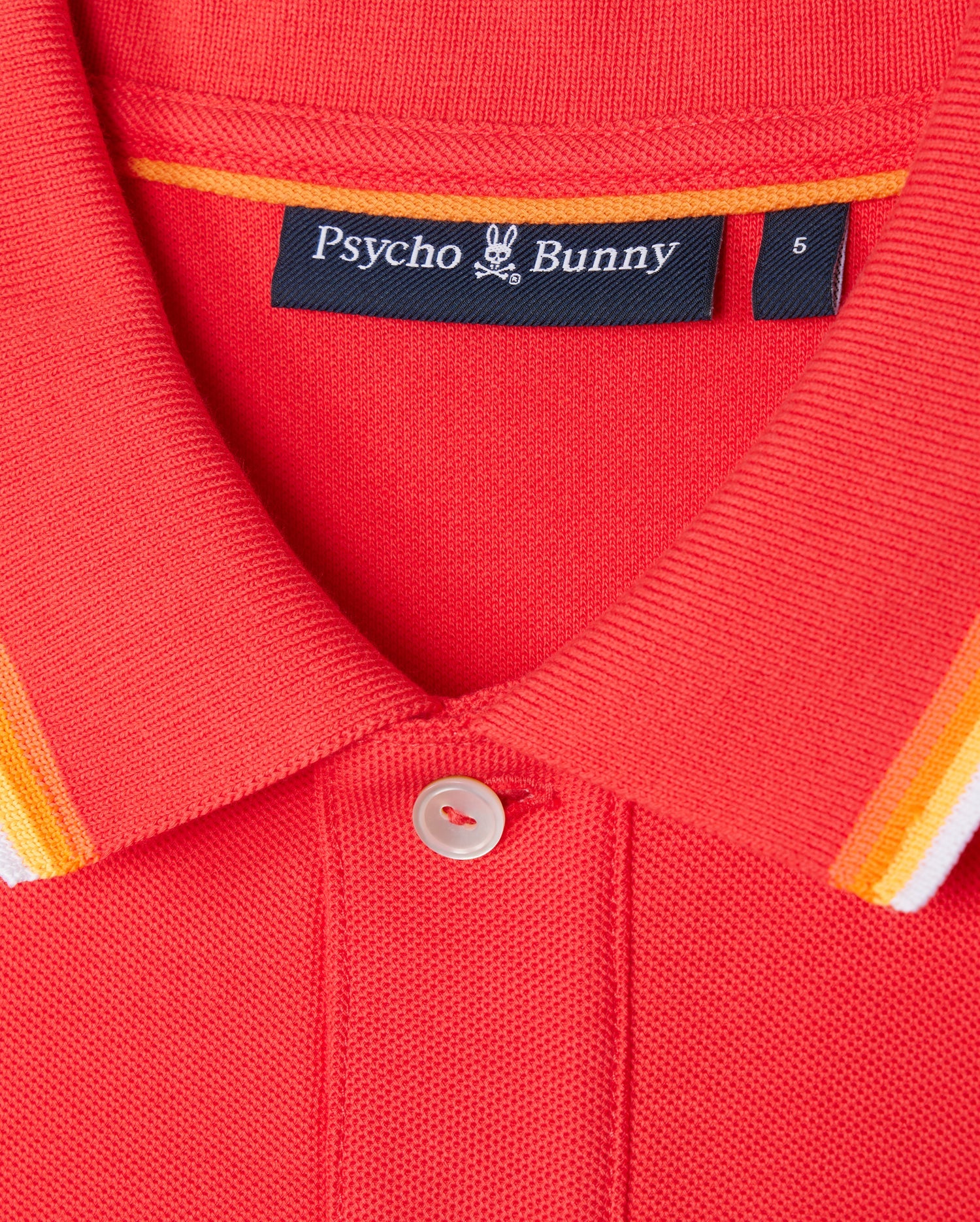 Close-up of the collar of the red Psycho Bunny MENS GRANBURY PIQUE POLO - B6K400C200, featuring a button at the top. The rib knit collar showcases orange, white, and yellow stripes along the edge. Inside the collar, a black label displaying the brand name and logo is visible.