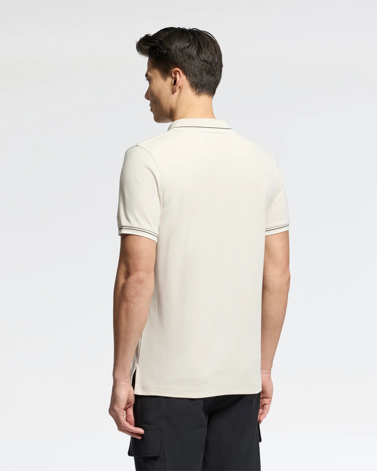 Facing away, a man dons a Psycho Bunny Men's Elliot Pique Polo (B6K505F200) made from soft Pima cotton. The shirt is light-colored with bold dark trim on the sleeves and collar, set against a plain, light gray background.