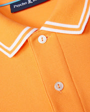 Close-up of a MENS BELTON PIQUE POLO - B6K575C200 showing part of the collar and buttons. The collar has white piping along the edges. A label from the brand "Psycho Bunny" is partially visible at the top, accompanied by their embroidered Bunny logo. The shirt fabric, made from Pima cotton, has a textured appearance.