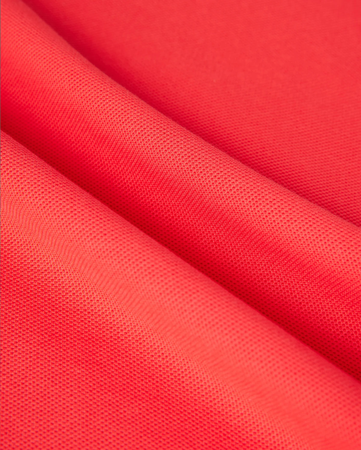 Close-up of vibrant red fabric with a subtle grid-like texture, folded in soft waves. The material appears smooth and slightly shiny, resembling diamond-knit Pima cotton, suitable for the MENS KAYDEN PIQUE POLO - B6K675C200 by Psycho Bunny.