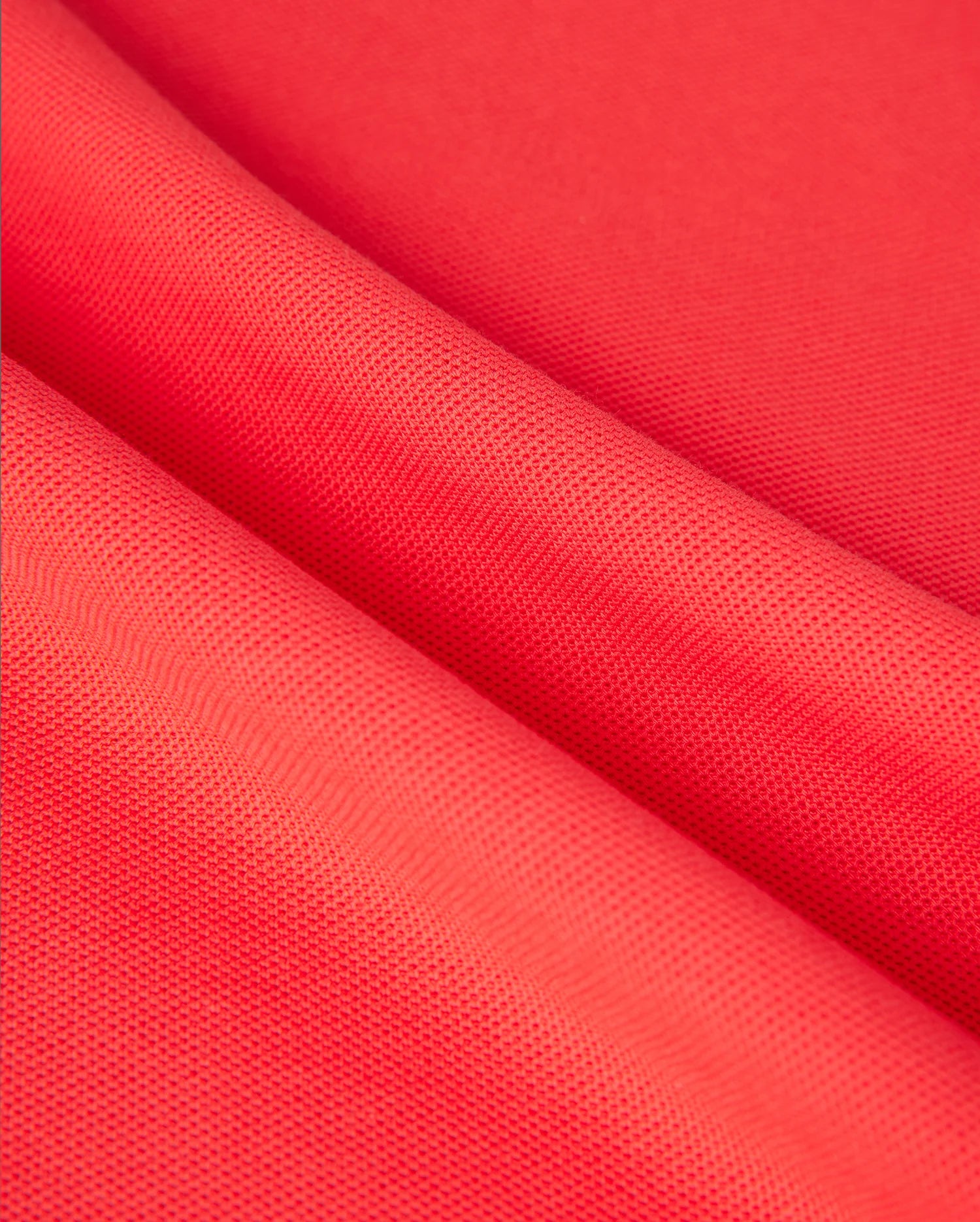 Close-up of vibrant red fabric with a subtle grid-like texture, folded in soft waves. The material appears smooth and slightly shiny, resembling diamond-knit Pima cotton, suitable for the MENS KAYDEN PIQUE POLO - B6K675C200 by Psycho Bunny.