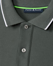 Close-up image of the Psycho Bunny Men's Kingston Pique Polo Shirt (B6K764D200) in vibrant green, crafted from Pima cotton with a ribbed collar and two buttons. The collar features a thin white trim, while an embroidered Bunny patch on the label inside reads "Psycho Bunny" with a logo of a bunny above the text.