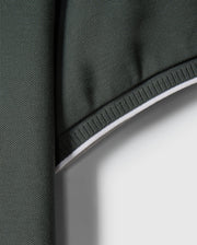 Close-up of a green Pima cotton fabric with a textured surface and white edge. The fabric appears to be folded at the top, creating a shadowed area. The edge is reinforced with white stitching, providing contrast against the dark green material – perfect for crafting a stylish MENS KINGSTON PIQUE POLO SHIRT - B6K764D200 by Psycho Bunny, perhaps with an embroidered Bunny patch.