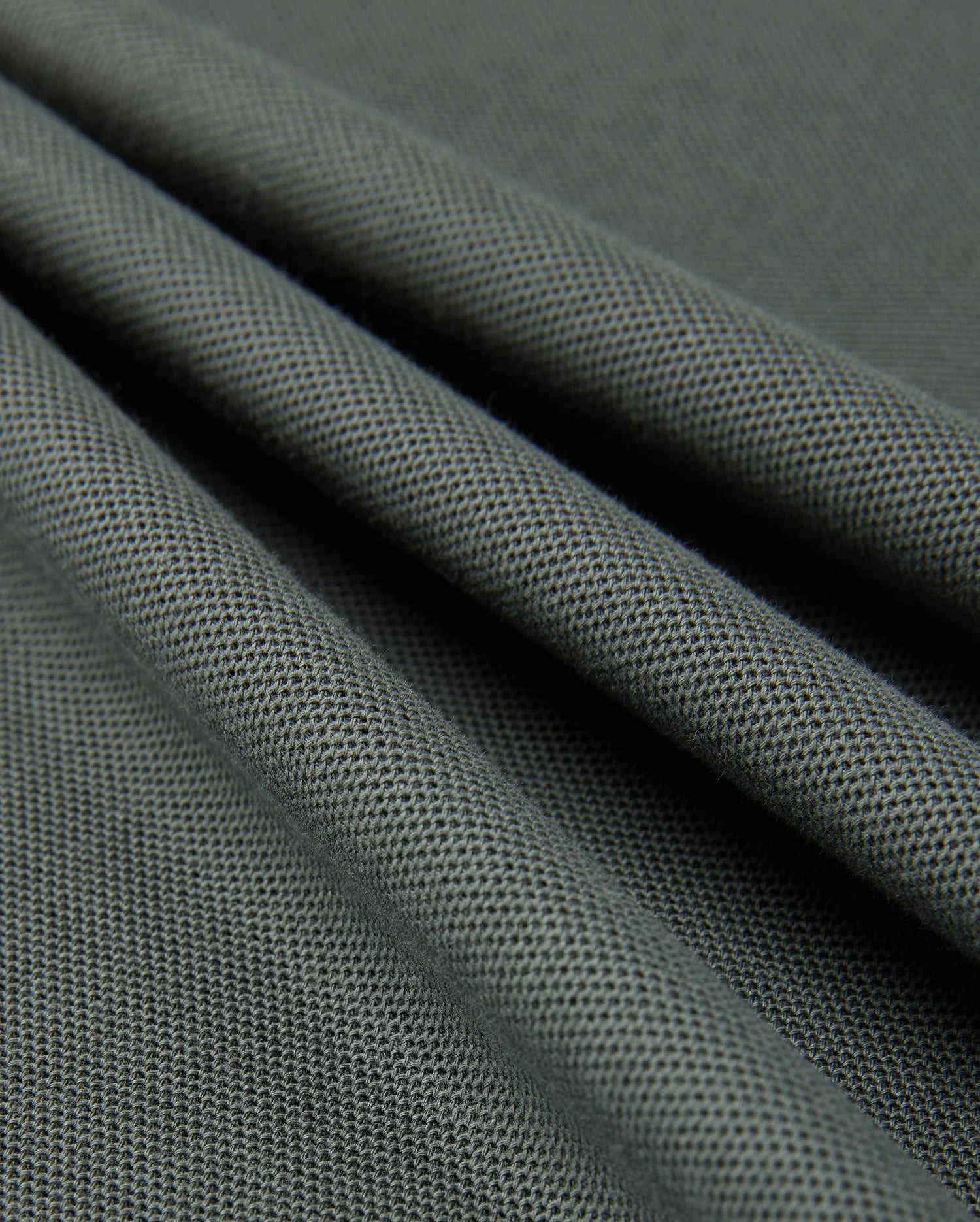 A close-up view of smooth, dark green Pima cotton with a fine, textured weave. The fabric is draped, creating gentle folds and shadows that highlight its soft and flexible nature, reminiscent of a luxurious Psycho Bunny MENS KINGSTON PIQUE POLO SHIRT - B6K764D200.