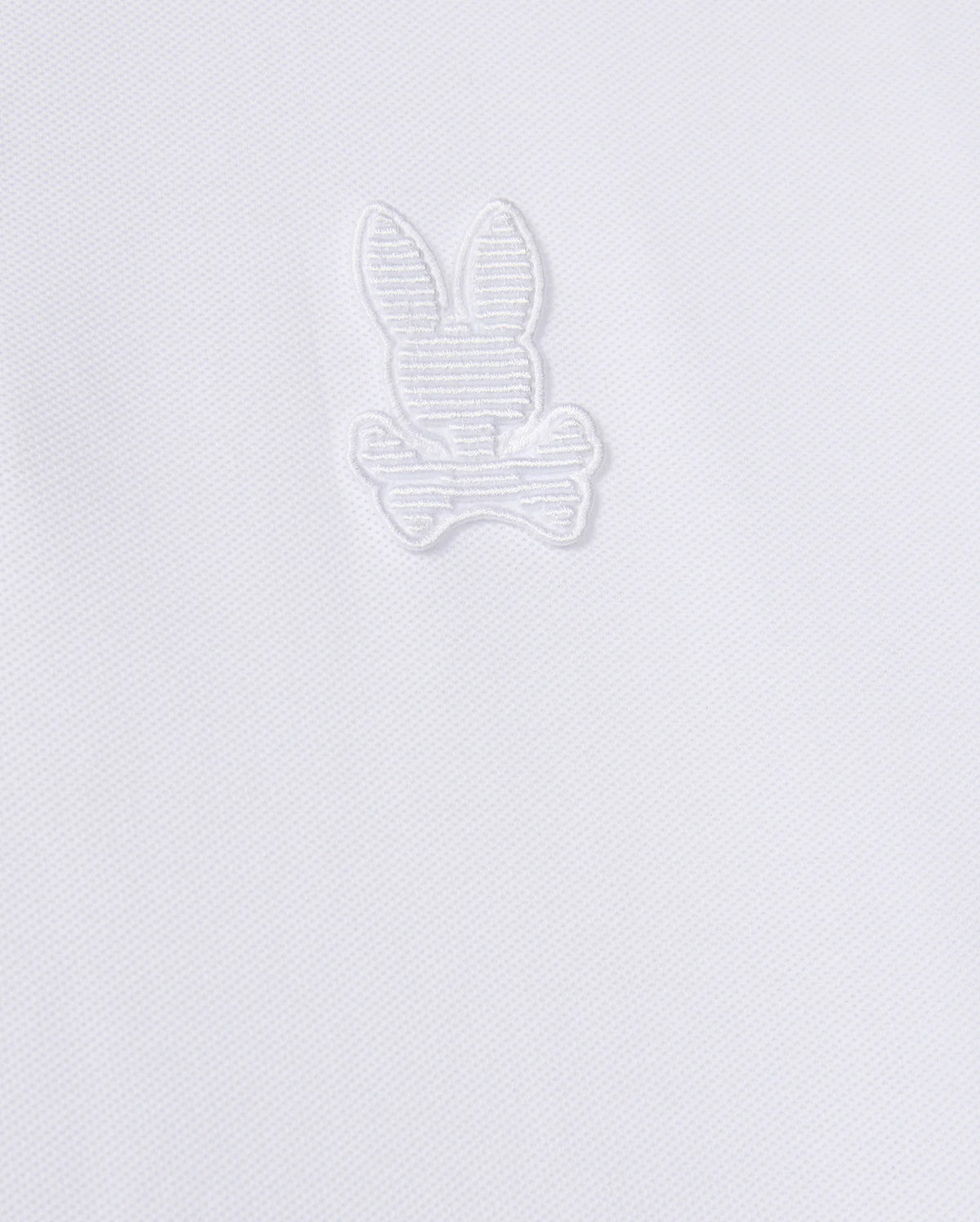 The Psycho Bunny MENS KINGSTON PIQUE POLO SHIRT - B6K764D200 is crafted from soft Pima cotton and features an embroidered Bunny patch with long ears, sitting above a pair of crossed bones. The design is stitched in matching white thread, blending subtly with the fabric.