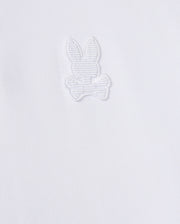 The Psycho Bunny MENS KINGSTON PIQUE POLO SHIRT - B6K764D200 is crafted from soft Pima cotton and features an embroidered Bunny patch with long ears, sitting above a pair of crossed bones. The design is stitched in matching white thread, blending subtly with the fabric.