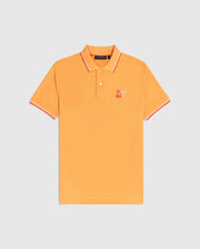 A bright orange Psycho Bunny MENS WINTON PIQUE POLO SHIRT - B6K841A2PC with a collar and short sleeves. Crafted from luxurious Peruvian Pima cotton in a diamond-knit piqué, it features red and white stripes on the collar and sleeve cuffs. An embroidered patch with a colorful cartoon character is visible on the left chest area.