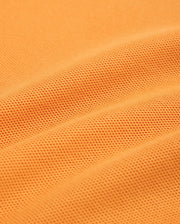 Close-up of a textured orange fabric with small, dotted patterns. The fabric, resembling Peruvian Pima cotton used in Psycho Bunny's MENS WINTON PIQUE POLO SHIRT - B6K841A2PC, appears to be slightly folded, creating gentle, curved lines and shadows across the surface.