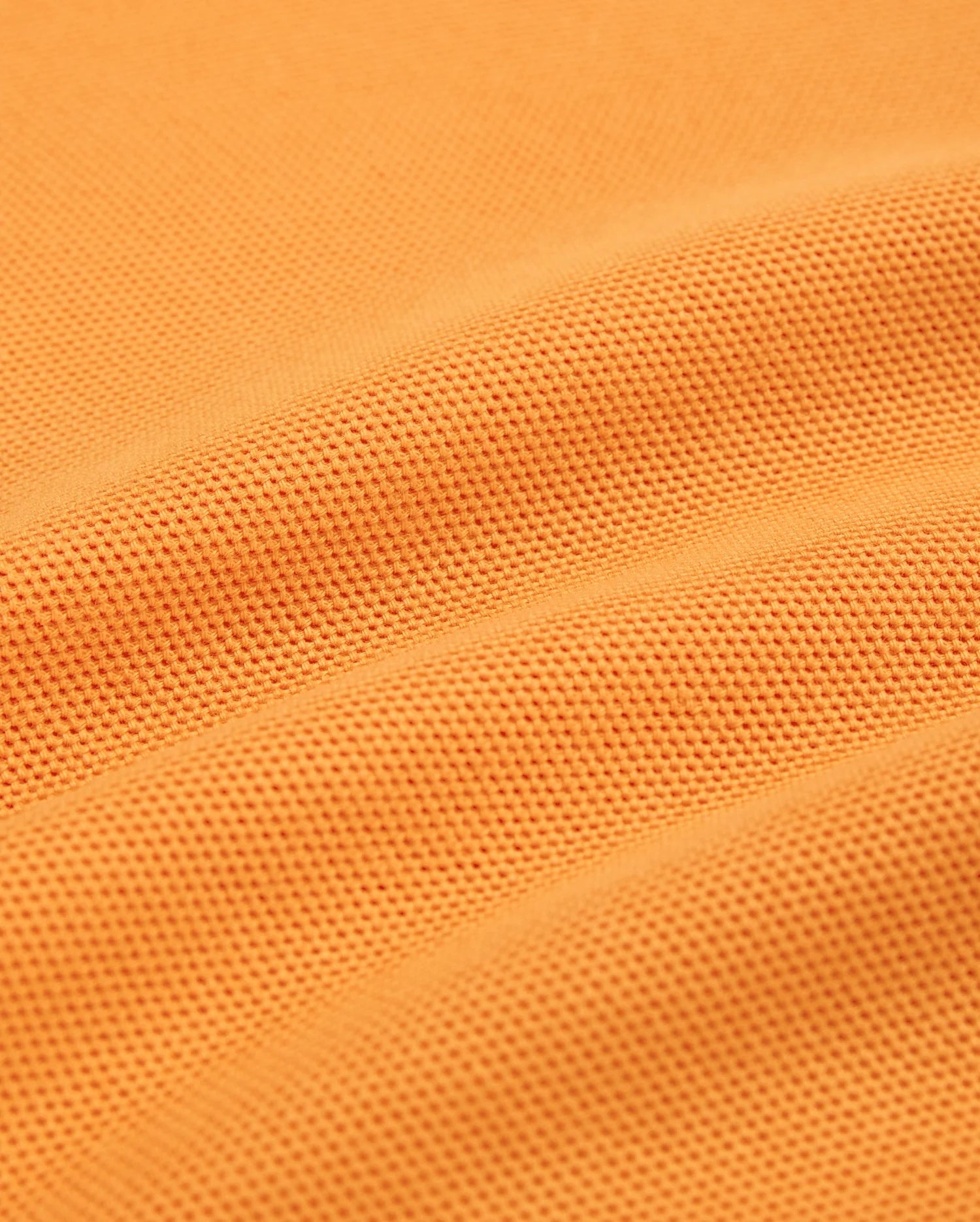 Close-up of a textured orange fabric with small, dotted patterns. The fabric, resembling Peruvian Pima cotton used in Psycho Bunny's MENS WINTON PIQUE POLO SHIRT - B6K841A2PC, appears to be slightly folded, creating gentle, curved lines and shadows across the surface.