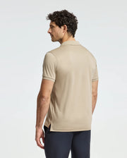 A man with curly hair, in a MENS BROADWAY PIMA INTERLOCK JOHNNY COLLAR POLO by Psycho Bunny and dark pants, stands facing away from the camera against a light grey background.
