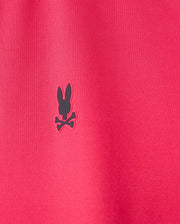 Close-up of a red fabric, typical of the breathable MENS BELLEVUE SPORT POLO SHIRT - B6K905D200 by Psycho Bunny, with a small black logo showcasing a rabbit head and crossbones.