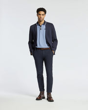A man stands wearing a navy blazer, the Psycho Bunny MENS KENT PIQUE POLO - B6K951D200 in light blue, dark trousers, and brown boots. He has his hands in his pockets and poses against a plain white background.