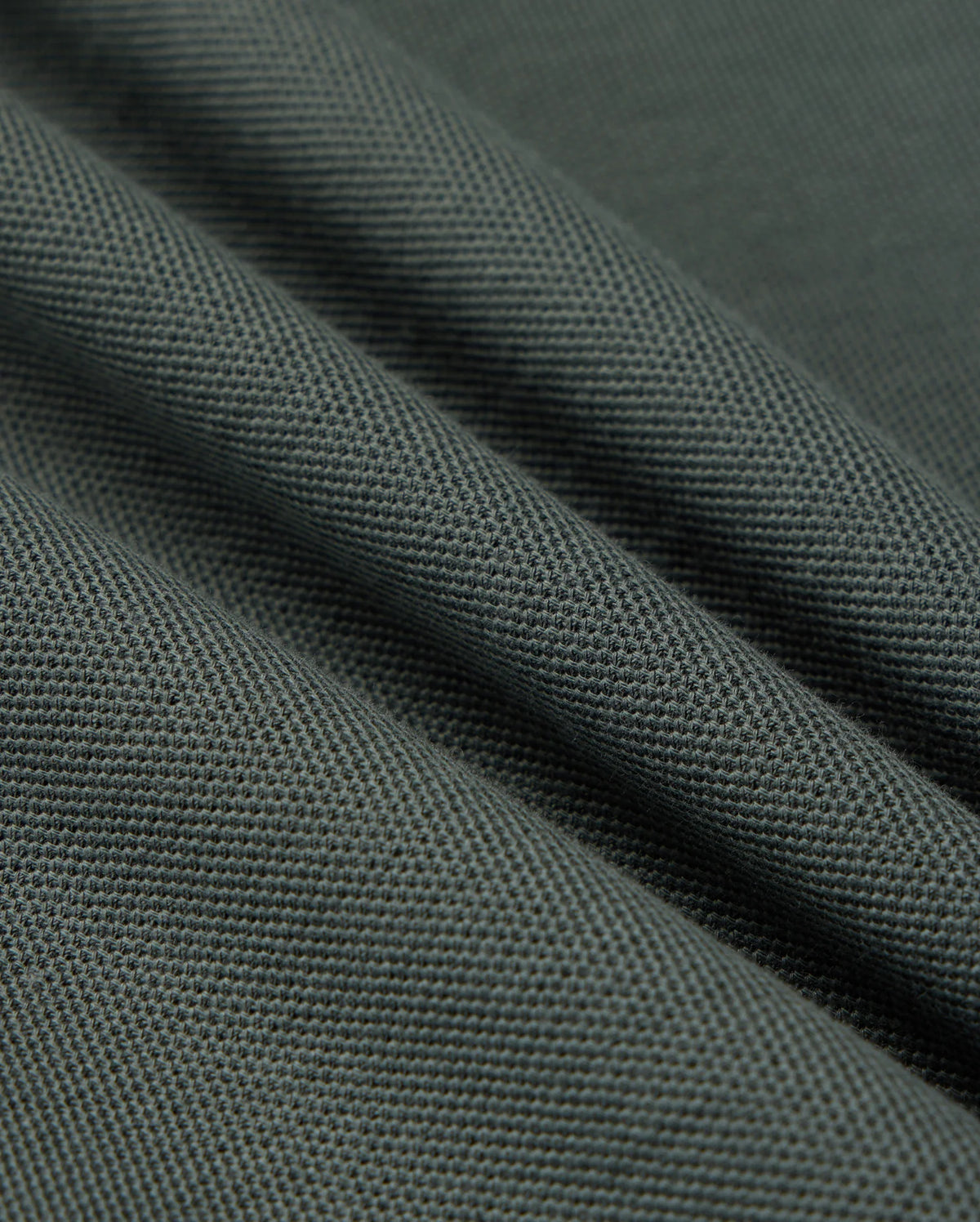 Close-up of the Psycho Bunny MENS KENT PIQUE POLO SHIRT in dark grey, featuring a textured weave pattern reminiscent of stylish polo fabric. The material is folded to form diagonal lines across the image, emphasizing its sturdy and dense quality.