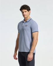A man with curly dark hair wears a Psycho Bunny regular fit light blue Pima cotton MENS MONROE PIQUE POLO - B6K964D200 featuring Mother-of-Pearl buttons and a small chest logo, paired with black pants, against a plain white background.