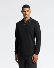 A person wearing the Psycho Bunny MENS CREEDE PIQUE JOHNNY COLLAR POLO - B6M265E200, made from soft Pima cotton with a white-trimmed Johnny collar, stands against a plain white background.