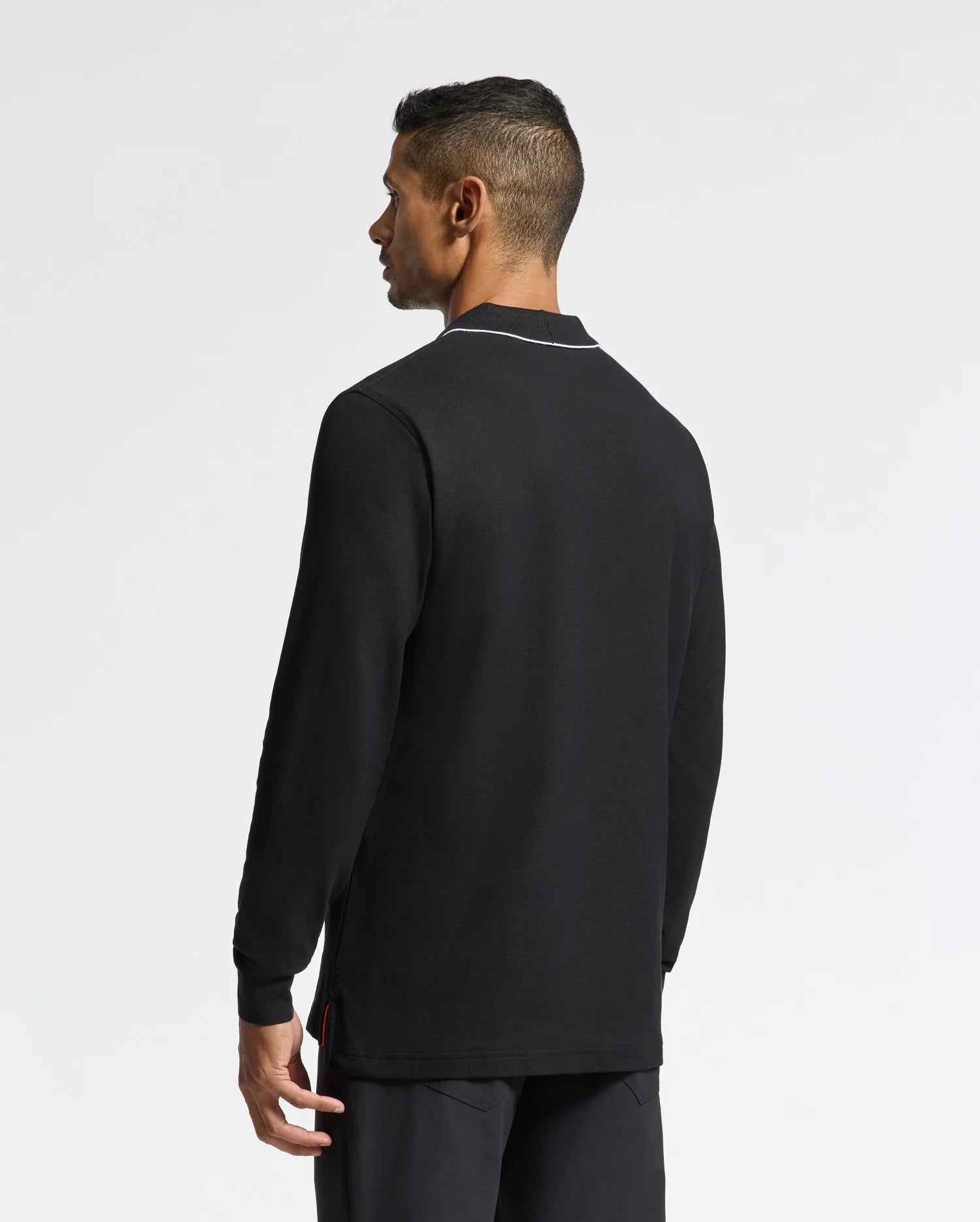 A man with short hair stands facing away, wearing a Psycho Bunny MENS CREEDE PIQUE JOHNNY COLLAR POLO - B6M265E200 in black. This long sleeve shirt, crafted from soft Pima cotton, features a unique Johnny collar accentuated by white lining, set against a plain white background.