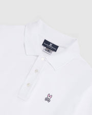 Introducing the MENS LONG SLEEVE CLASSIC POLO - B6M658ARPC from Psycho Bunny. This men's white polo shirt features a classic collar and three-button placket on the front, crafted from 100% Pima cotton in a diamond-knit piqué fabric for added texture. The left chest area displays a small, embroidered pink bunny with black crossbones logo. An inner neck label reads "Psycho Bunny." The backdrop is light gray.