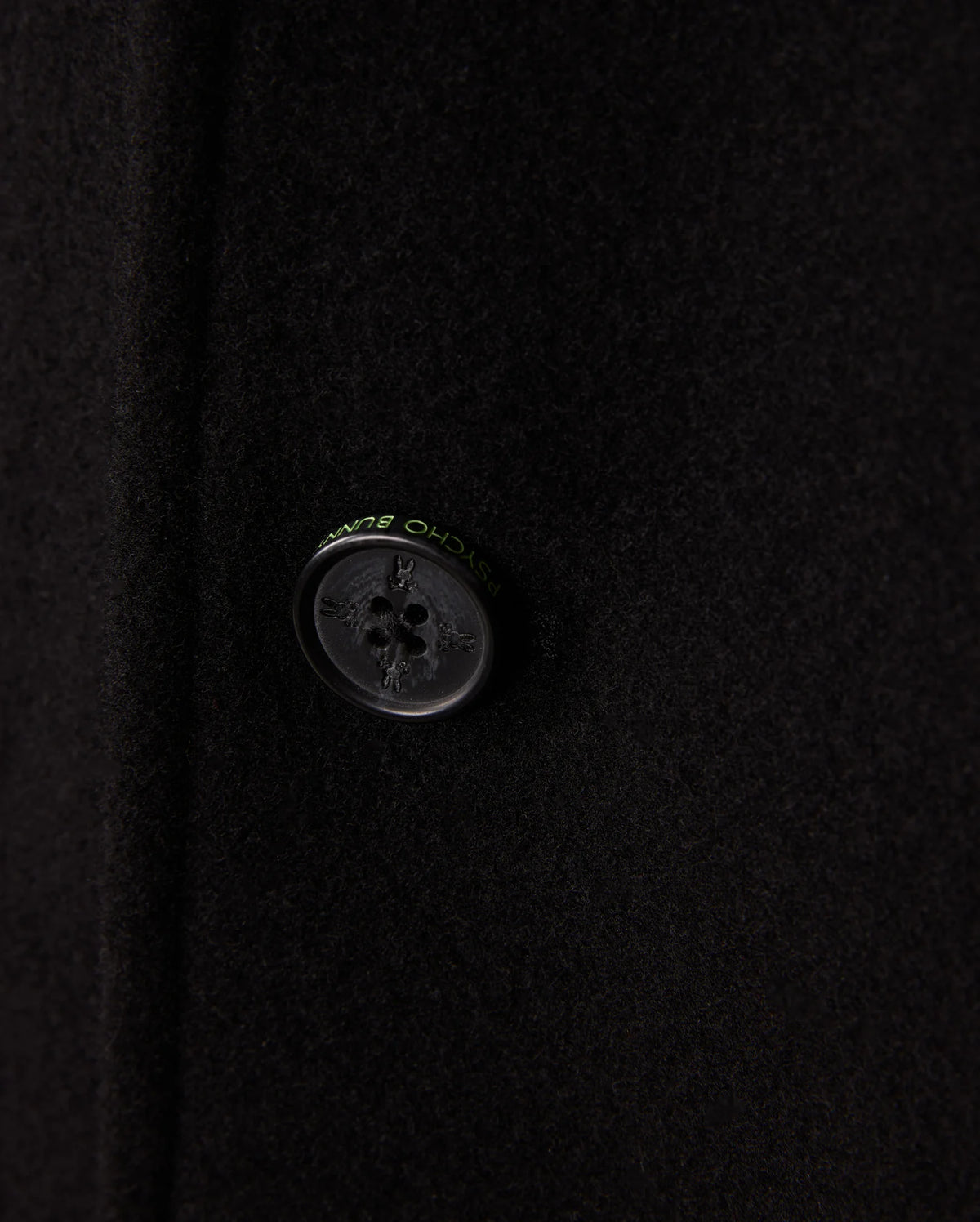 Zoom in on the refined black button of the Psycho Bunny Men's Stafford Wool Blend Coat - B6N551D200. This elegant winter coat boasts a four-hole button with discreet text around it and its wool blend fabric offers a soft, slightly textured look.