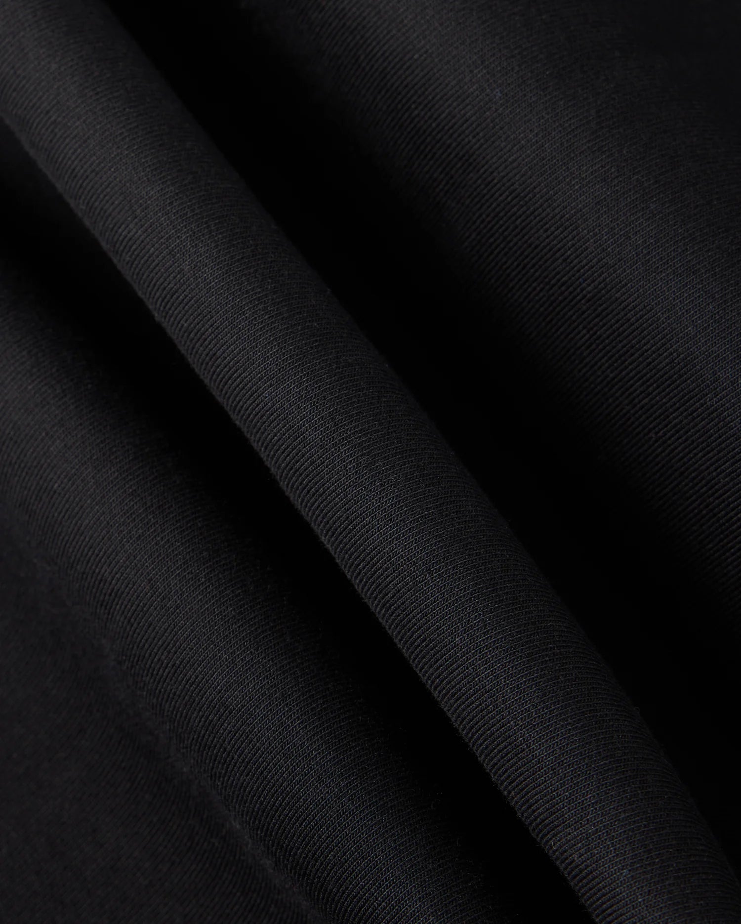 Close-up of the MENS TRAVIS TRACK PANT - B6P143D200 fabric by Psycho Bunny, showcasing a smooth and slightly shiny texture with subtle diagonal lines. Crafted from high-quality cotton-blend material, it appears gently folded, creating soft creases and a streamlined appearance.