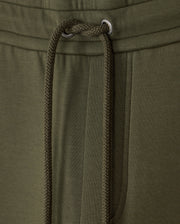 Close-up of the waistband and drawstring of a pair of olive green MENS TRAVIS TRACK PANT - B6P143D200 by Psycho Bunny. The image highlights the texture of the high-quality cotton-blend fabric and the metal eyelets through which the drawstring is threaded. A pocket is partially visible on the right side.