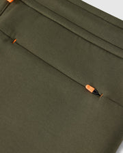 Close-up of an olive green fabric, typical of the Psycho Bunny MENS TRAVIS TRACK PANT - B6P143D200, featuring a hidden zipper pocket. The orange zipper pull is partially visible, blending seamlessly with the high-quality cotton-blend material. The fabric has a smooth texture and neat stitching along the edges.