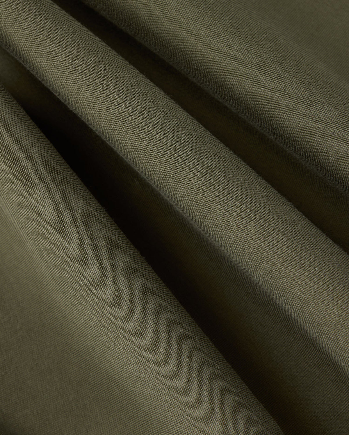 Close-up view of folded dark green fabric with visible texture and subtle shadows, showcasing the smooth surface and soft draping folds of high-quality cotton-blend material found in the Psycho Bunny MENS TRAVIS TRACK PANT - B6P143D200.