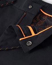 Close-up of the MENS LLOYD CARGO JOGGER - B6P159B200 by Psycho Bunny, featuring black cargo jogger pants with orange stitching and an orange-lined waistband. The interior fabric showcases an orange design with cartoon characters. These pants are designed with two silver buttons, a zippered opening equipped with snap closures, and elasticized cuffs for a snug fit.