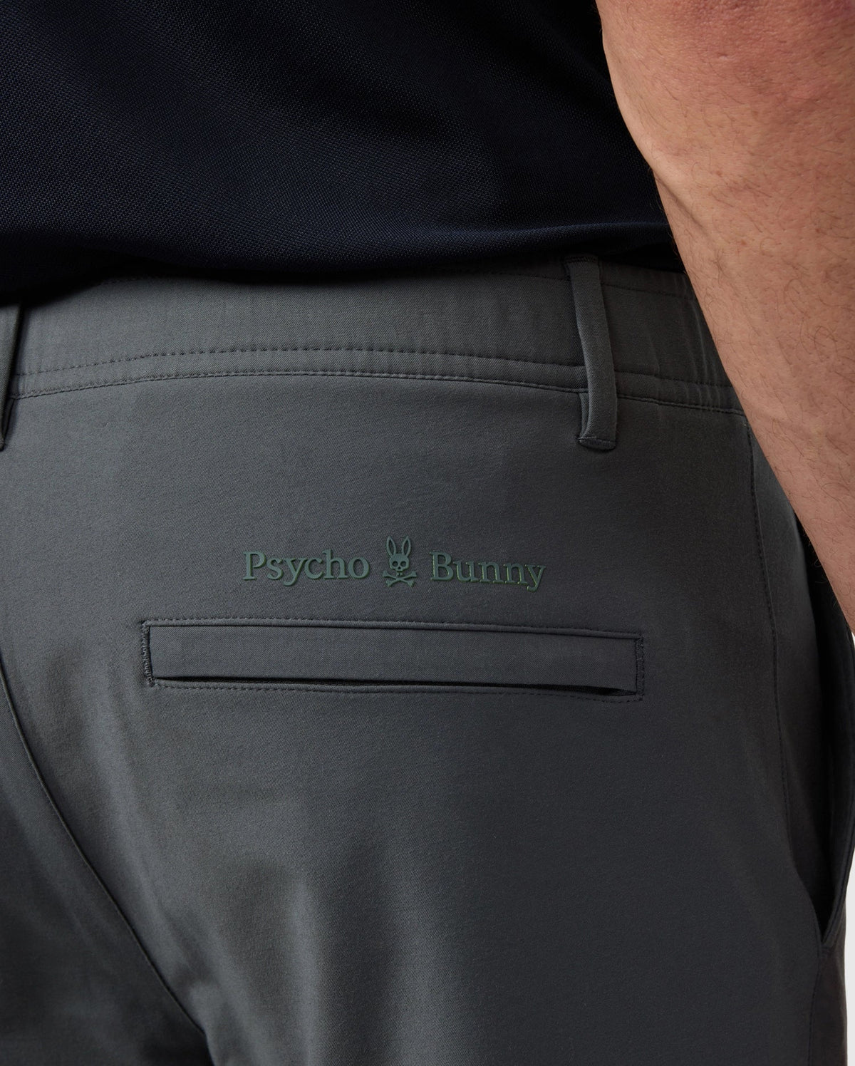 Close-up of the back pocket of Psycho Bunny men's Madison commuter pant showing the "psycho bunny" logo embroidered above the pocket.