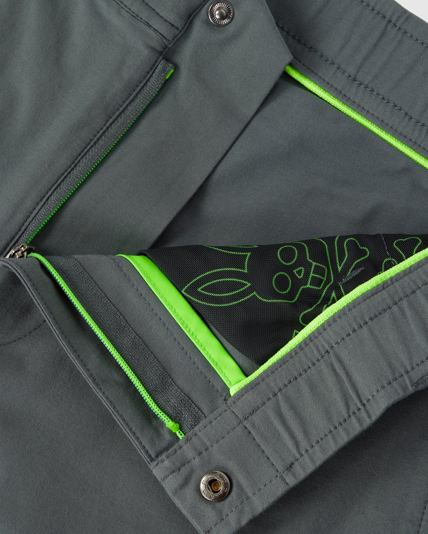 Close-up of a Psych Bunny MENS MADISON COMMUTER PANT - B6P395Z1WB showing interior detail with a neon green zipper and lining, and a decorative sketch of flower and leaves in white on a stretch woven material background.