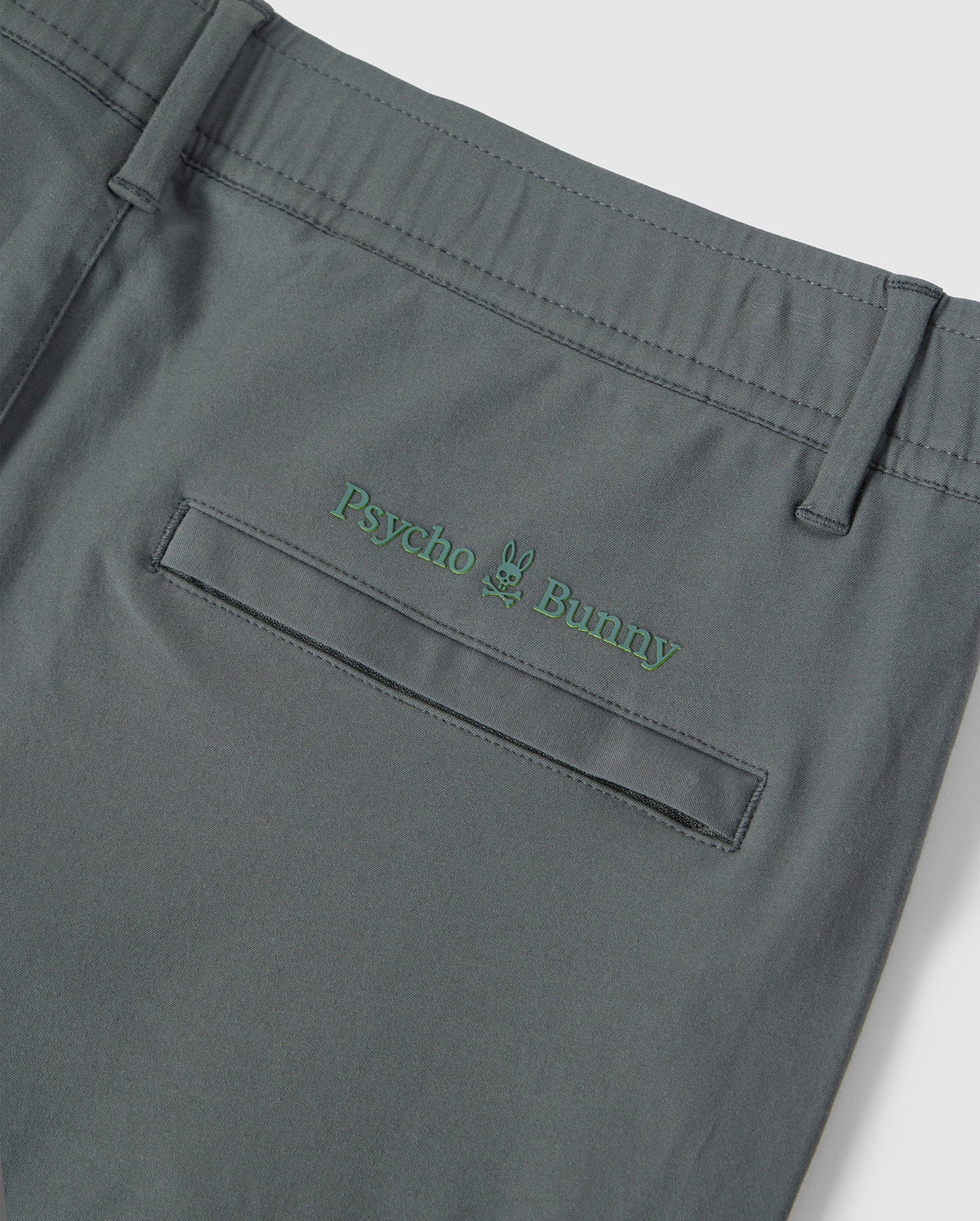 Close-up of the back pocket of Psycho Bunny's Mens Madison Commuter Pant with the embroidered Bunny logos and a small green bunny graphic above the text.