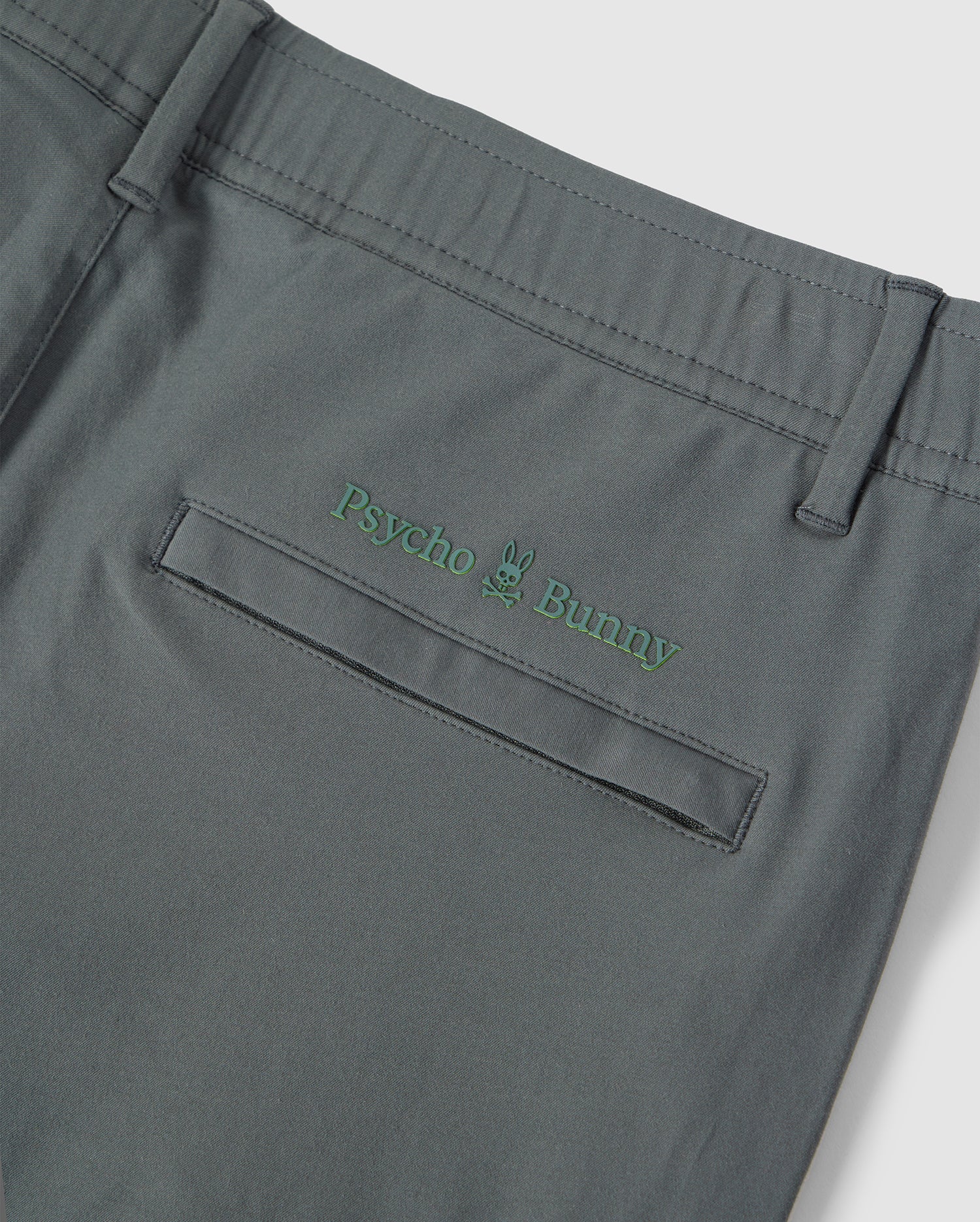Close-up of the back pocket of Psycho Bunny's Mens Madison Commuter Pant with the embroidered Bunny logos and a small green bunny graphic above the text.