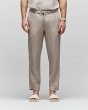 A person wears Psycho Bunny MENS FATE LINEN DRAWSTRING PANT (B6P471C200) and cream slide sandals, standing with hands relaxed at their sides against a plain light background.