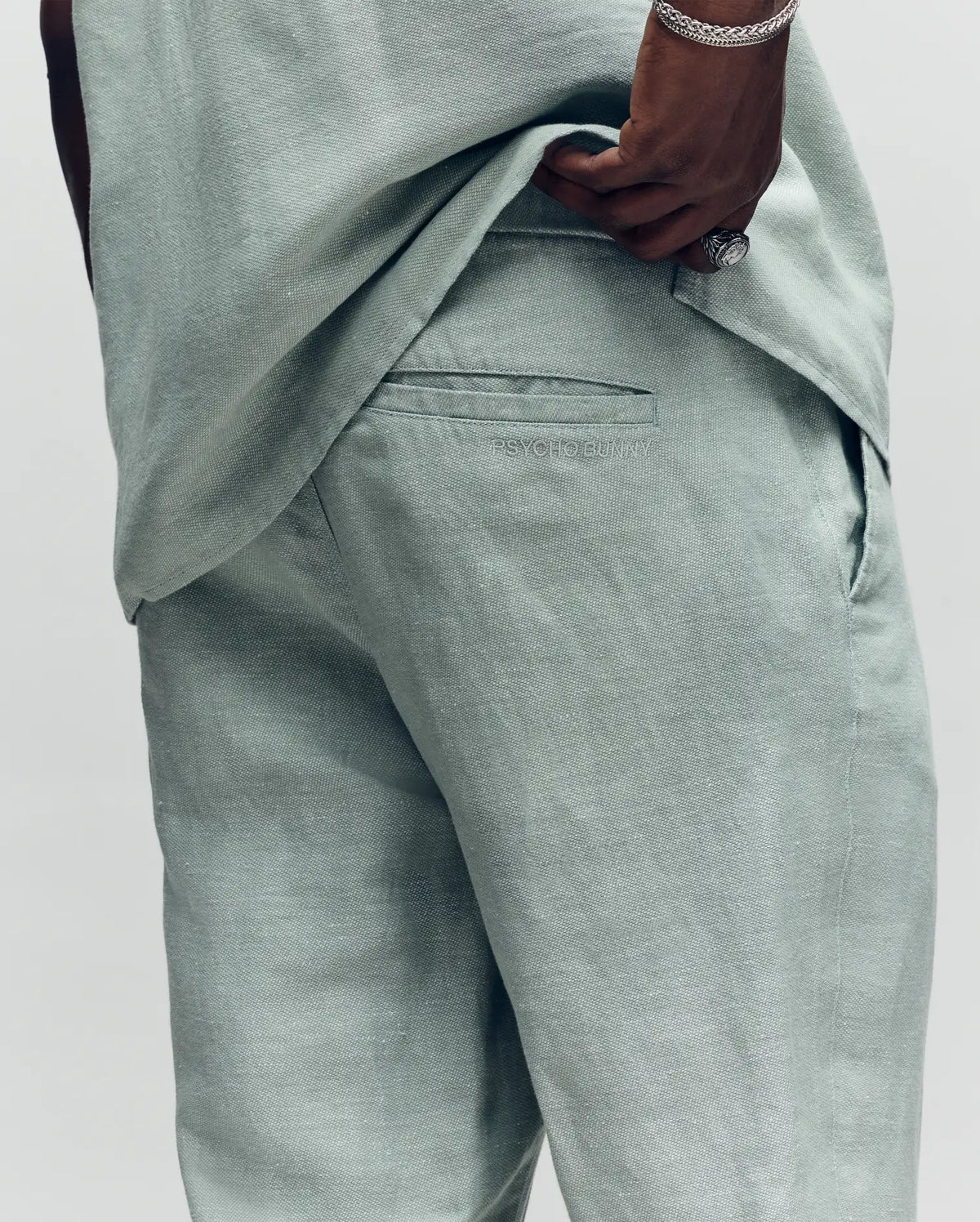 Psycho Bunny light green linen pants with a relaxed fit, visible textured fabric, back pocket, and subtle Psycho Bunny logo embroidery above the back pocket.