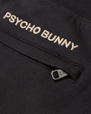 Close-up of a black cotton-blend garment displaying the embroidered text "Psycho Bunny" in white. Below the text, there's a partially open small zipper pocket with a branded logo on the zipper pull, ideal for pairing with premium bottoms such as the MENS JAMES PREMIUM SWEATPANT - B6P791D200.