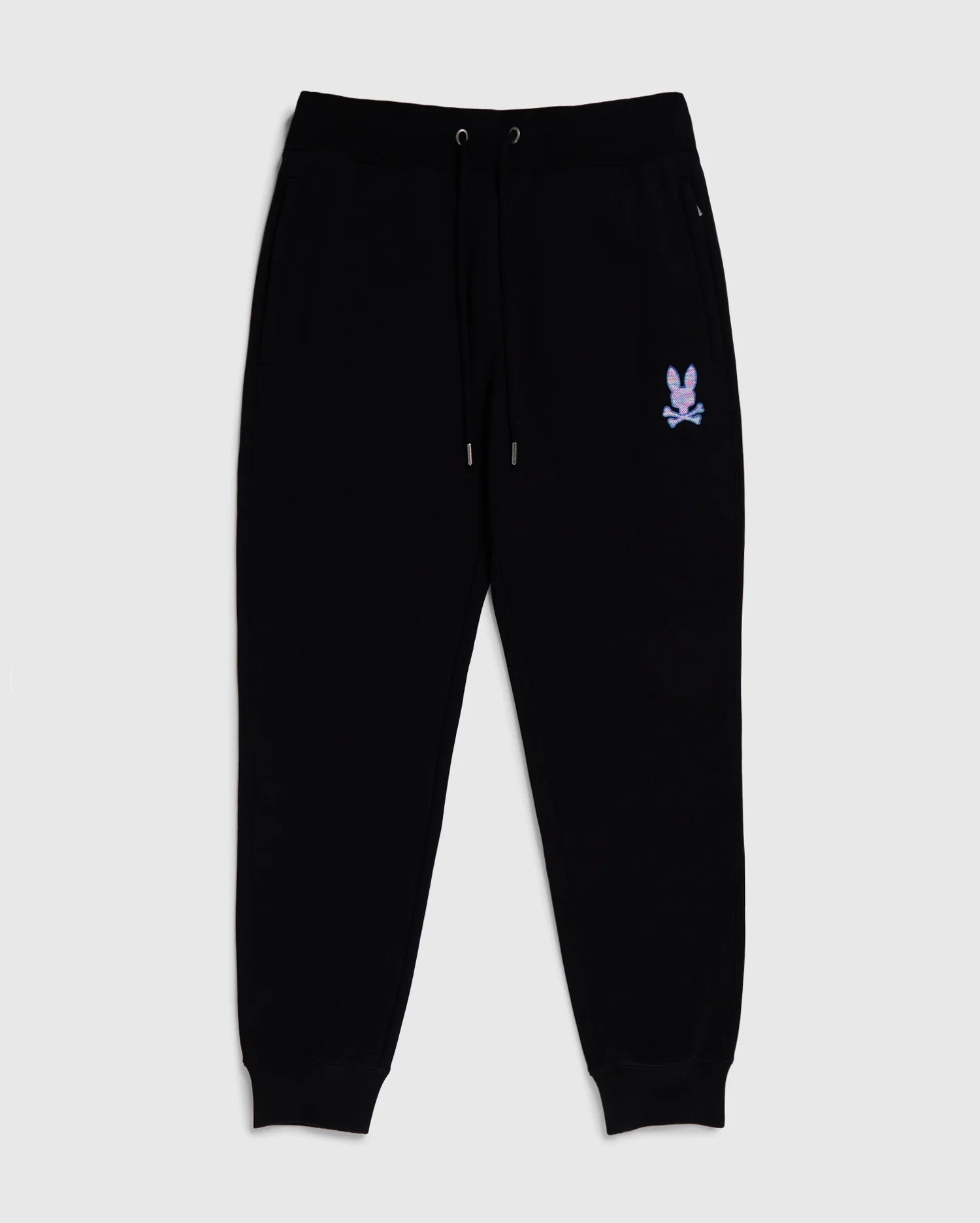 Black jogger pants with an elastic waistband and drawstrings, featuring two side pockets. Made from 100% cotton, these MENS SANTA CRUZ SWEATPANT - B6P843A2FT by Psycho Bunny blend comfort and style effortlessly. There is a small design of a bunny with crossbones in white near the left pocket and ribbed cuffs at the ankles.