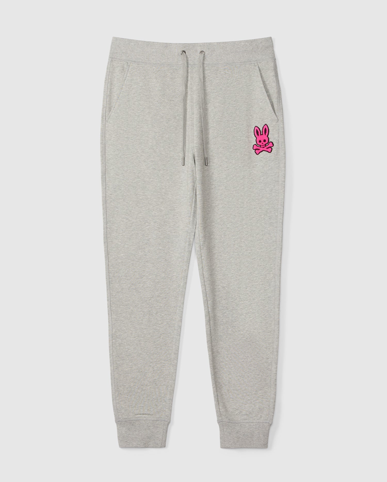The SCOTT CHENILLE PATCH SWEATPANT by Psycho Bunny, product code B6P856D200, features a pink bunny and crossbones design on the left upper leg. It includes an elastic waistband with drawstrings and ankle cuffs.