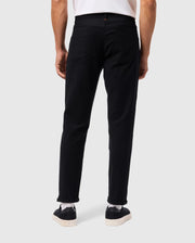A person wearing a regular fit white shirt, MENS HAYS TWILL PANT by Psycho Bunny in black, and black sneakers with white soles stands with their back facing the camera. The background is a plain light gray.