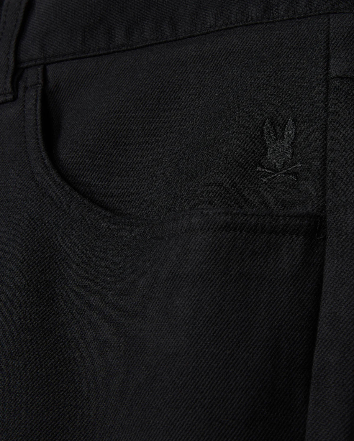Close-up of a black denim pocket on the Psycho Bunny MENS HAYS TWILL PANT - B6P894D200, featuring an embroidered rabbit's head with crossed bones beneath it. This subtle design detail enhances this regular fit piece, crafted from a cotton-blend twill.
