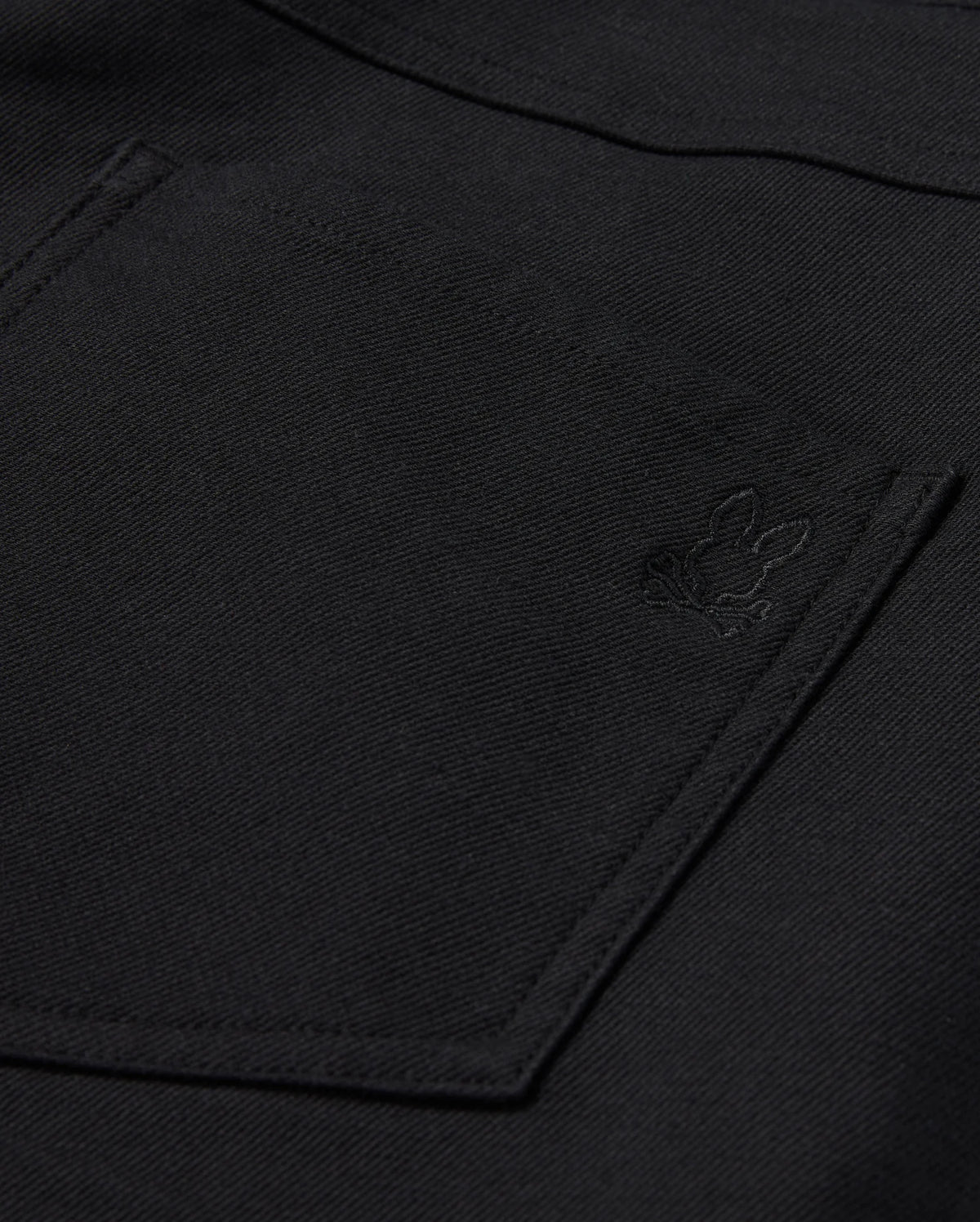 Close-up of Psycho Bunny's MENS HAYS TWILL PANT, showcasing a black fabric featuring a pocket and an embroidered bunny design in the corner. The texture is slightly rough, suggesting a durable cotton-blend twill material.