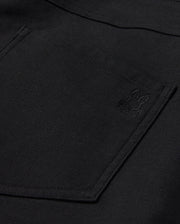Close-up of Psycho Bunny's MENS HAYS TWILL PANT, showcasing a black fabric featuring a pocket and an embroidered bunny design in the corner. The texture is slightly rough, suggesting a durable cotton-blend twill material.