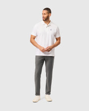 A person wearing a regular fit white polo shirt and Psycho Bunny's gray MENS HAYS TWILL PANT - B6P894D200 stands against a light gray background. They are wearing white shoes, have short hair and a beard, and the polo shirt features a small logo on the chest.